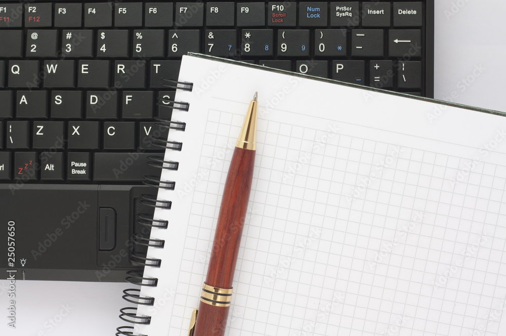Pen and spiral notepad on black laptop keyboard Pen and spiral notepad on black laptop keyboard