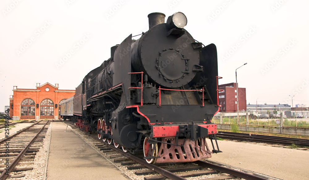 Fototapeta premium Steam locomotive beside a railway station platform. Retro train.