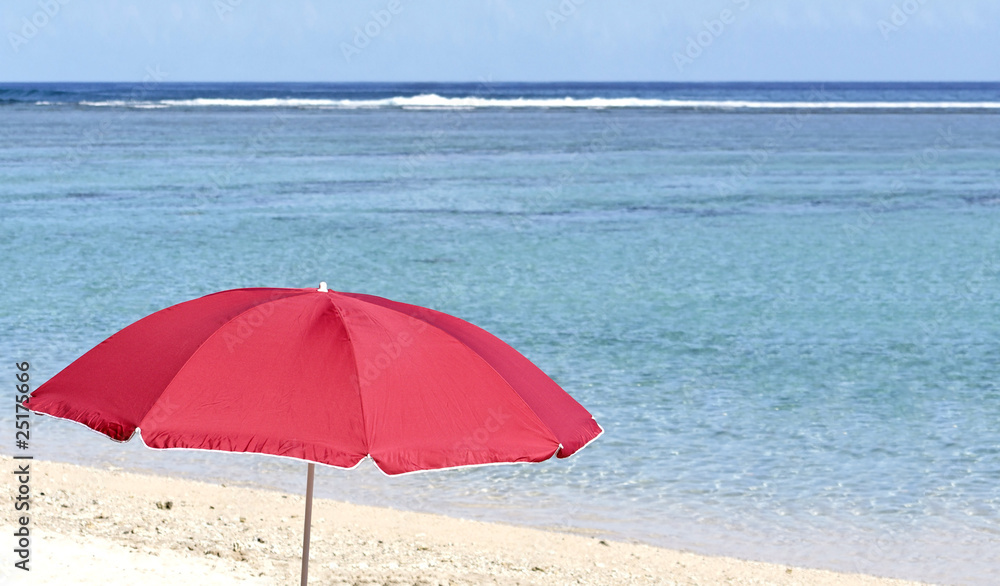 Parasol rouge sur plage de sable blanc