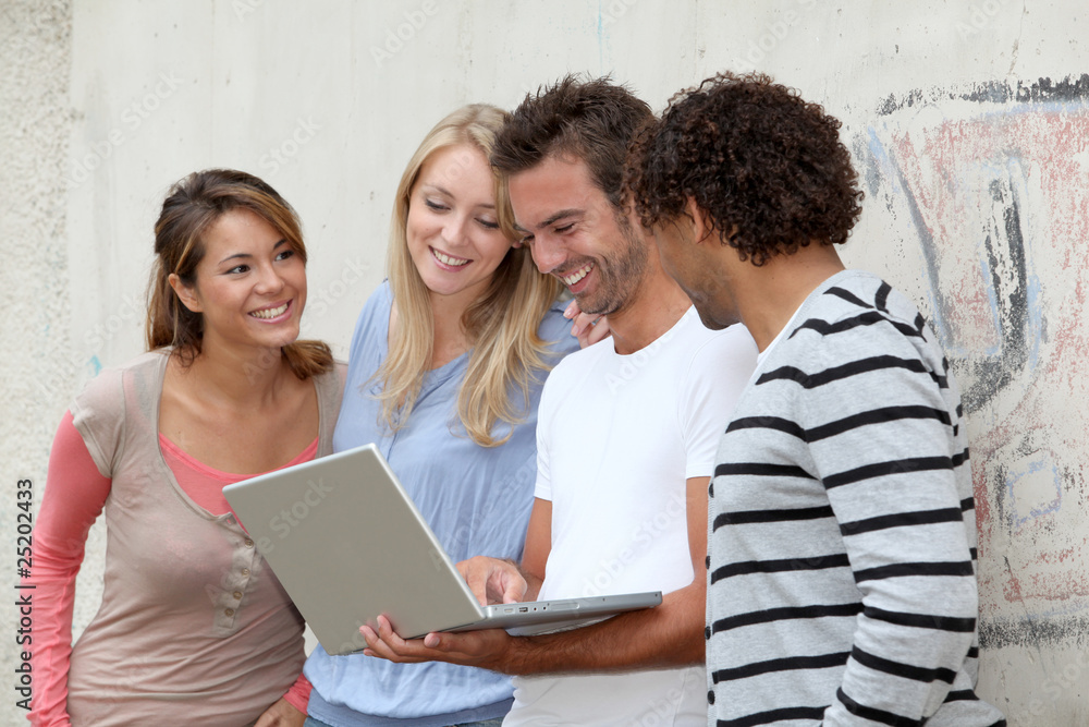 Group of friends standing against wall with laptop computer Group of friends standing against wall with laptop computer