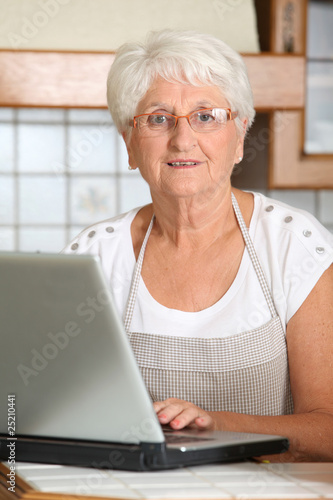 Elderly woman in kitchen with laptop computer