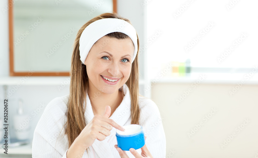 Delighted young woman putting cream on her face in the bathroom Delighted young woman putting cream on her face in the bathroom