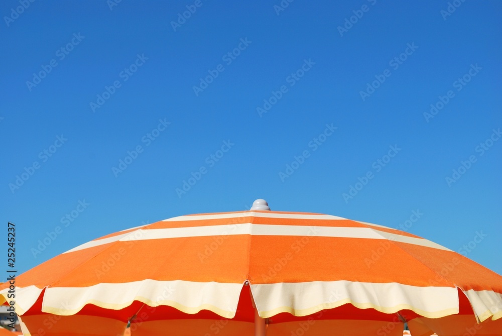 Orange striped beach umbrella on blue sky, Rimini, Italy