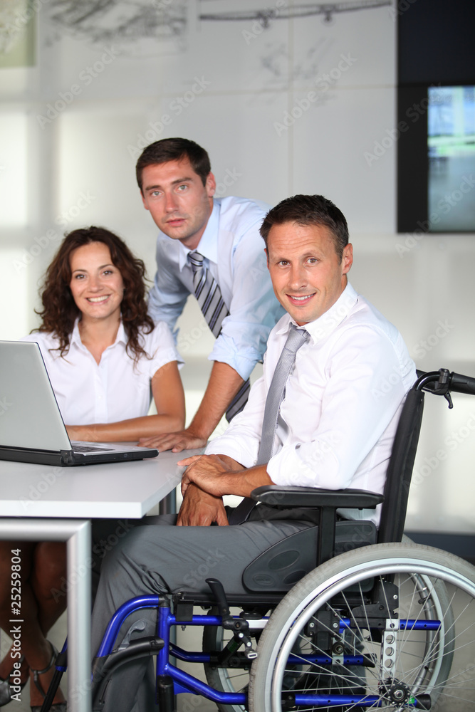 Businessman in wheelchair working in the office with colleagues Businessman in wheelchair working in the office with colleagues