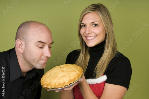 Man smelling pie held by woman