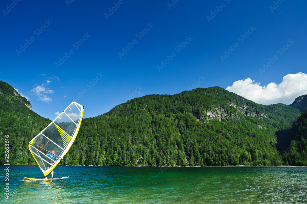 Fototapeta premium Windsurfer on mountain lake. Copyspace on blue sky.