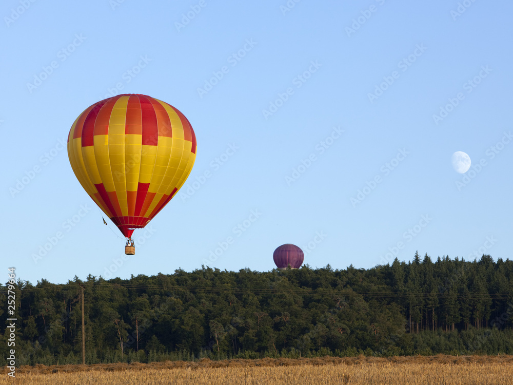 Naklejka premium Heißluftballons und Mond über Feld und Wald