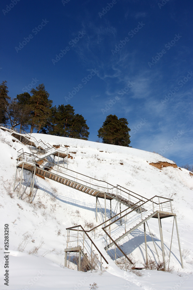 Stairs with landing against a snow slope against pines Stairs with landing against a snow slope against pines
