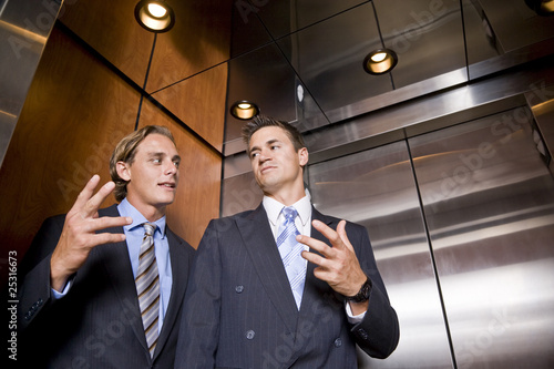 Fototapeta Businessmen riding in elevator conversing