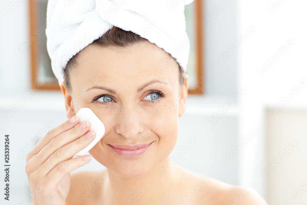 Young woman putting cream on her face wearing a towel in the bat Young woman putting cream on her face wearing a towel in the bat