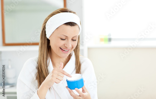 Slika na platnu Radiant woman putting cream on her face wearing a headband in th