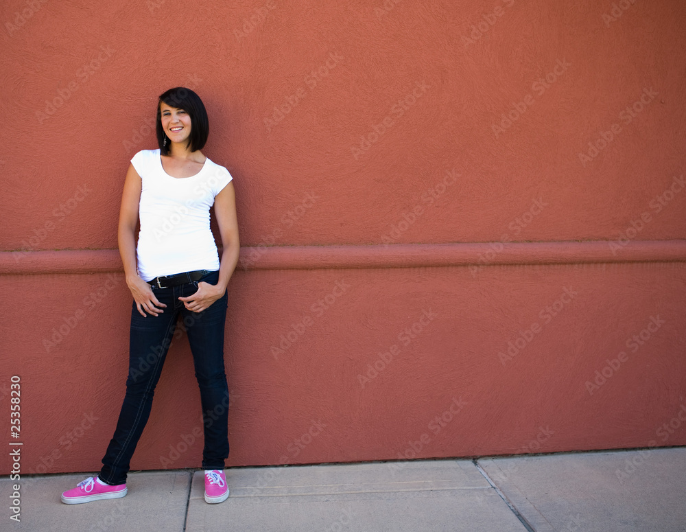 Obraz premium Beautiful young brunette girl on red wall with hands in pockets
