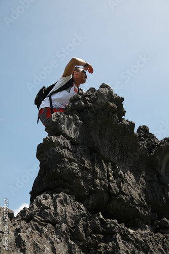 A man hiking with a bag on his back celebrates on top of a rock with his hands raised in triumph