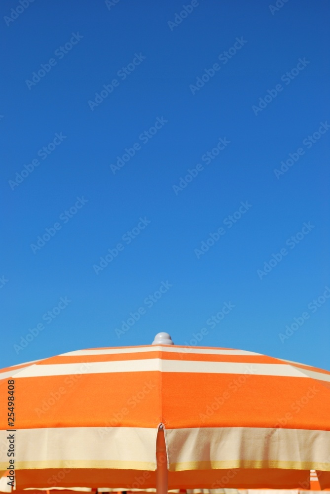 Orange striped beach umbrella on blue sky, Rimini, Italy