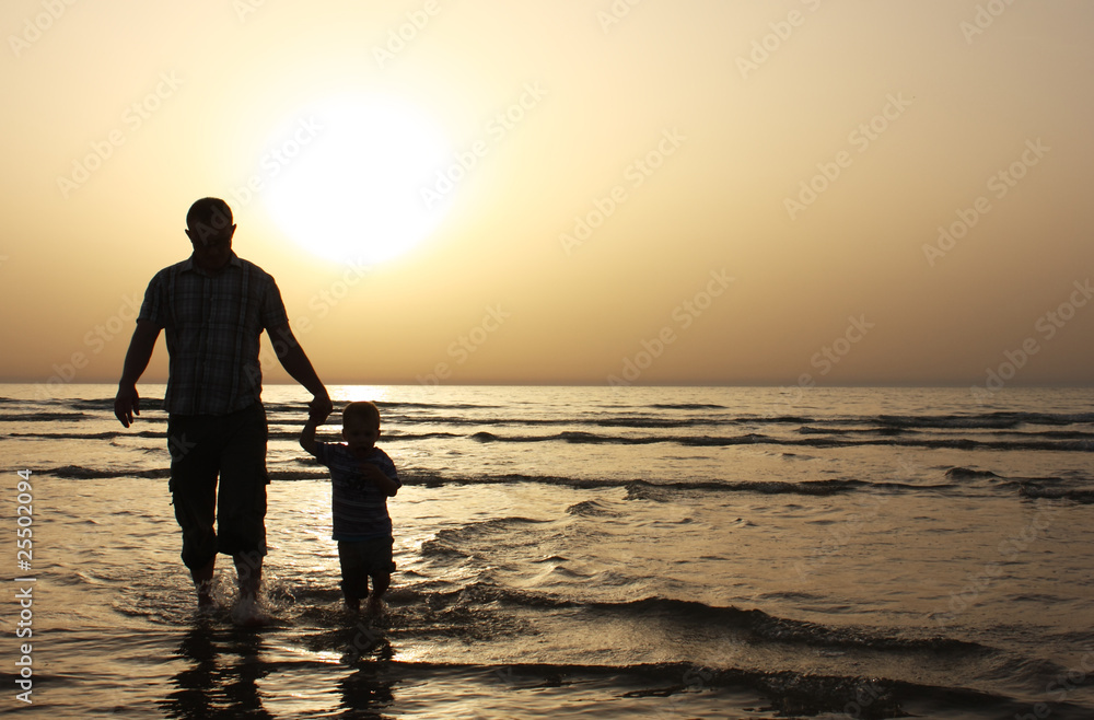 Silhouette image of father and his child by the sea shore, sunse
