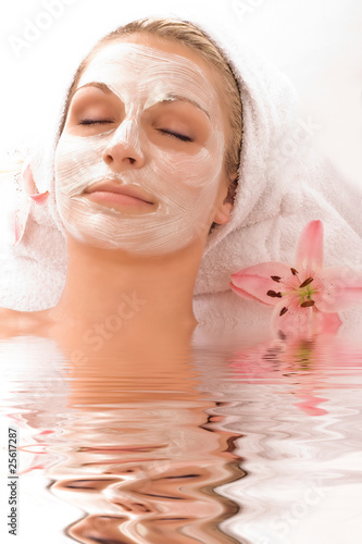 junge Frau mit Gesichtsmaske im Wasser mit rosa Blüte photo