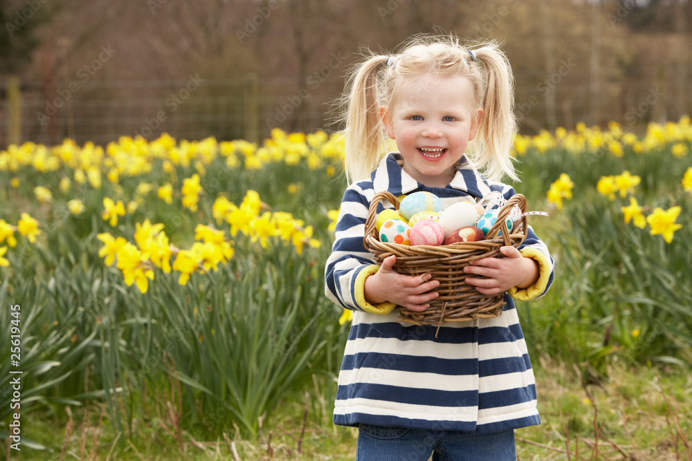 Fototapeta premium Young Girl Holding Basket Of Decorated Eggs In Daffodil Field