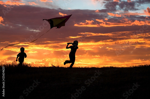 A brother and sister getting a kite to fly suring sunset.