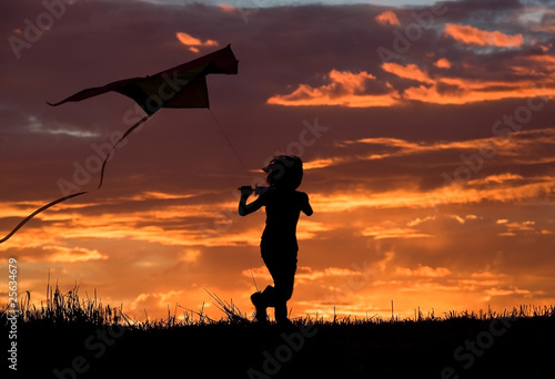 A young girl runs to try and fly her kite at sunset.
