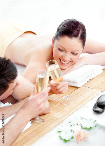 Loving young couple drinking champagne lying on a massage table