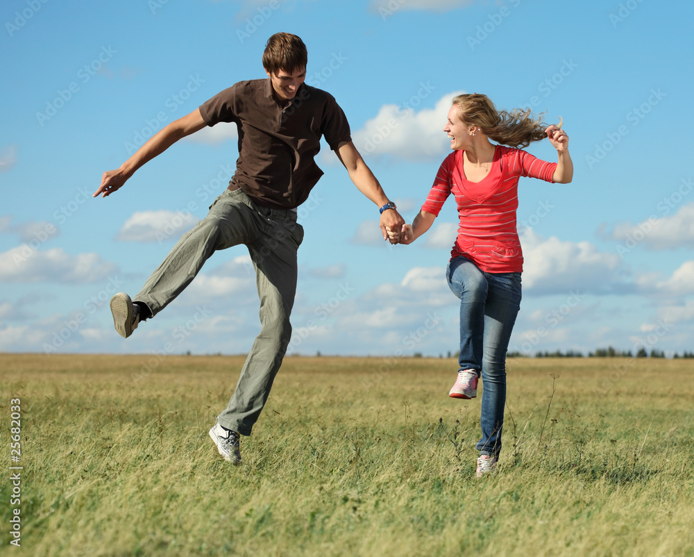 Young laughing couple jumping on meadow holding each other hands Young laughing couple jumping on meadow holding each other hands
