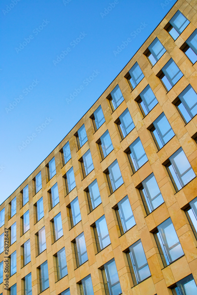 Diagonal view of office building facade underneath a clear blue sky which is reflected in the windows forming a rising pattern Diagonal view of office building facade underneath a clear blue sky which is reflected in the windows forming a rising pattern