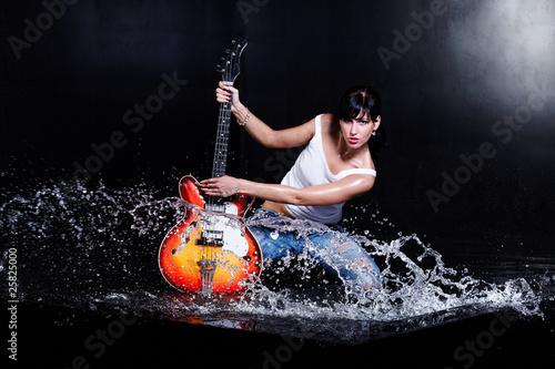 Rock-n-roll girl playing a guitar in water on black