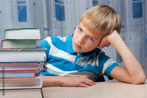 Sad boy at the table with a stack of books