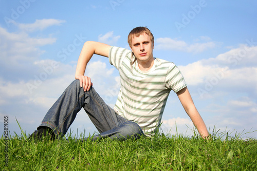 young handsome man lying on summer lawn, hand on knee, looking a