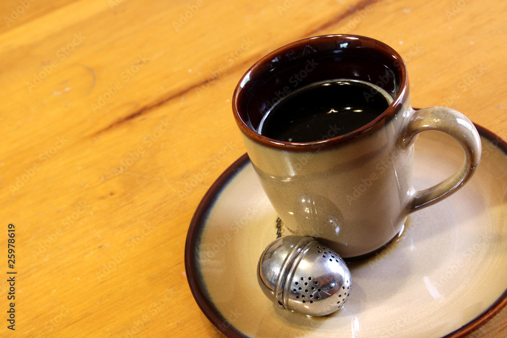Obraz premium A tea strainer sitting next to a mug of hot freshly brewed tea..