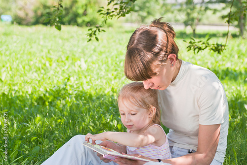 Mother and daughter sitting on the grass and looking book