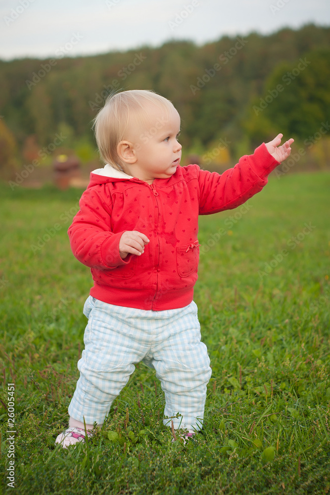 young cheerful baby stay on the grass in park with hand up young cheerful baby stay on the grass in park with hand up