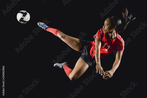 Mixed race soccer player kicking soccer ball in mid-air