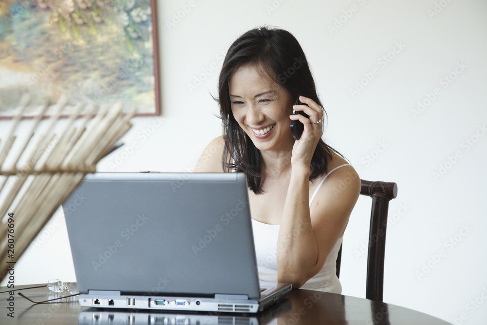 Japanese woman using laptop and talking on cell phone Japanese woman using laptop and talking on cell phone
