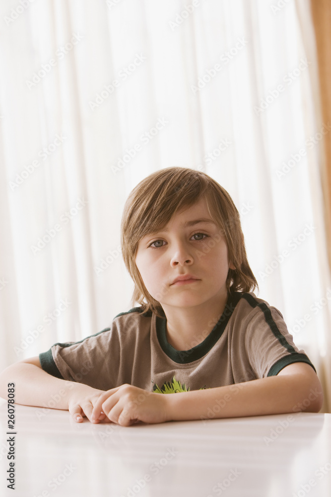 Hispanic boy sitting at table and looking serious Hispanic boy sitting at table and looking serious