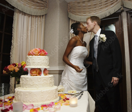 Bride and groom kissing next to wedding cake
