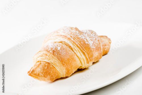 fresh croissant on white plate with powdered sugar