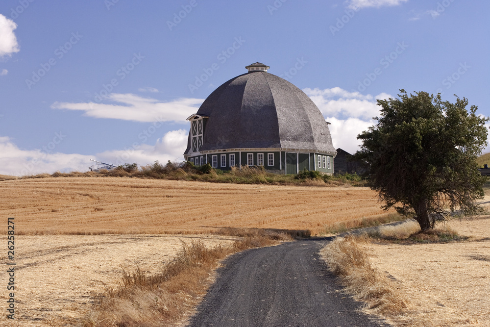Obraz premium A round barn stands on a hill at the end of a lane.