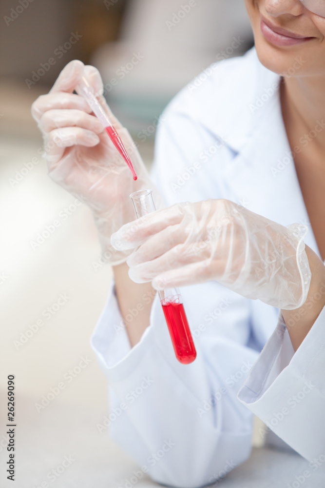 Close-up of a smiling scientist holding a pipette and a test tub Close-up of a smiling scientist holding a pipette and a test tub