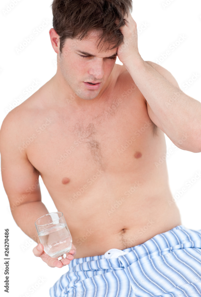 Fototapeta premium Dejected young man sitting on his bed and holding a glass of wat