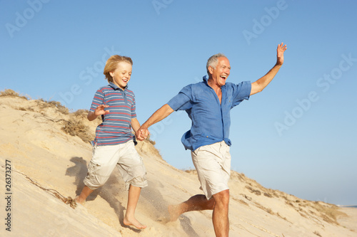 Grandfather And Grandson Enjoying Beach Holiday Running Down Dun