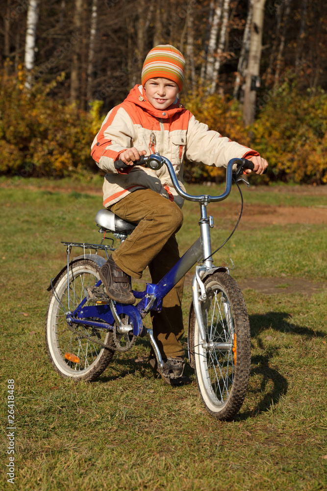 Boy on bicycle in autumn park on sunny day.