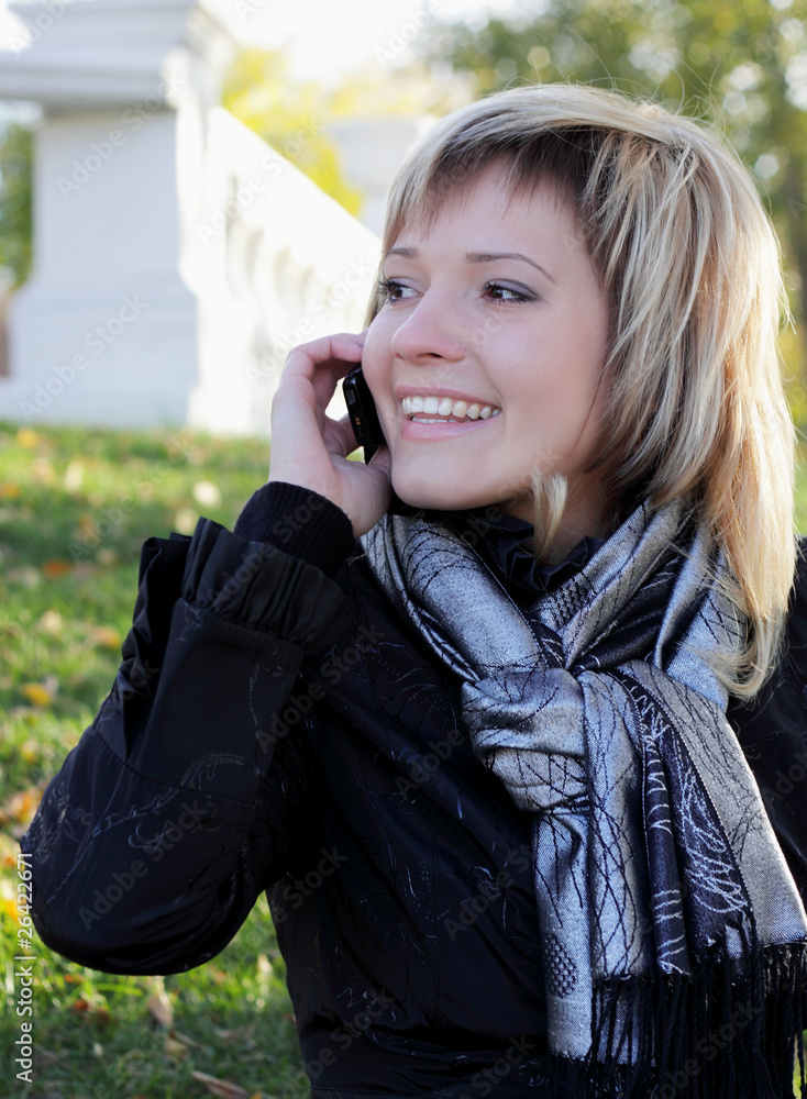 a charming young woman in autumn park talking on the phone