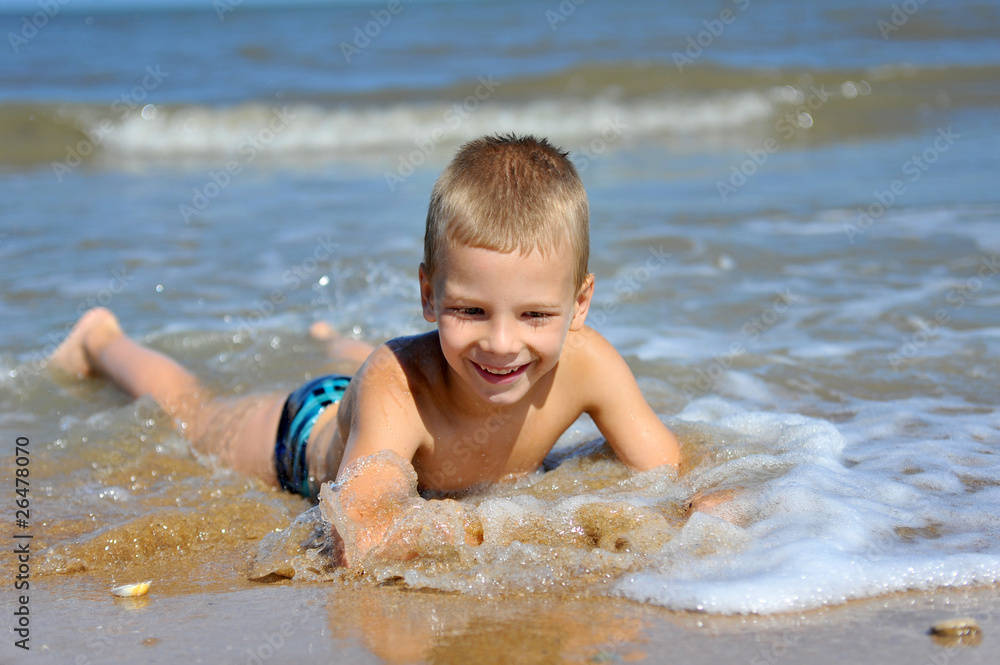 Smiling boy lying in water at the beach Smiling boy lying in water at the beach
