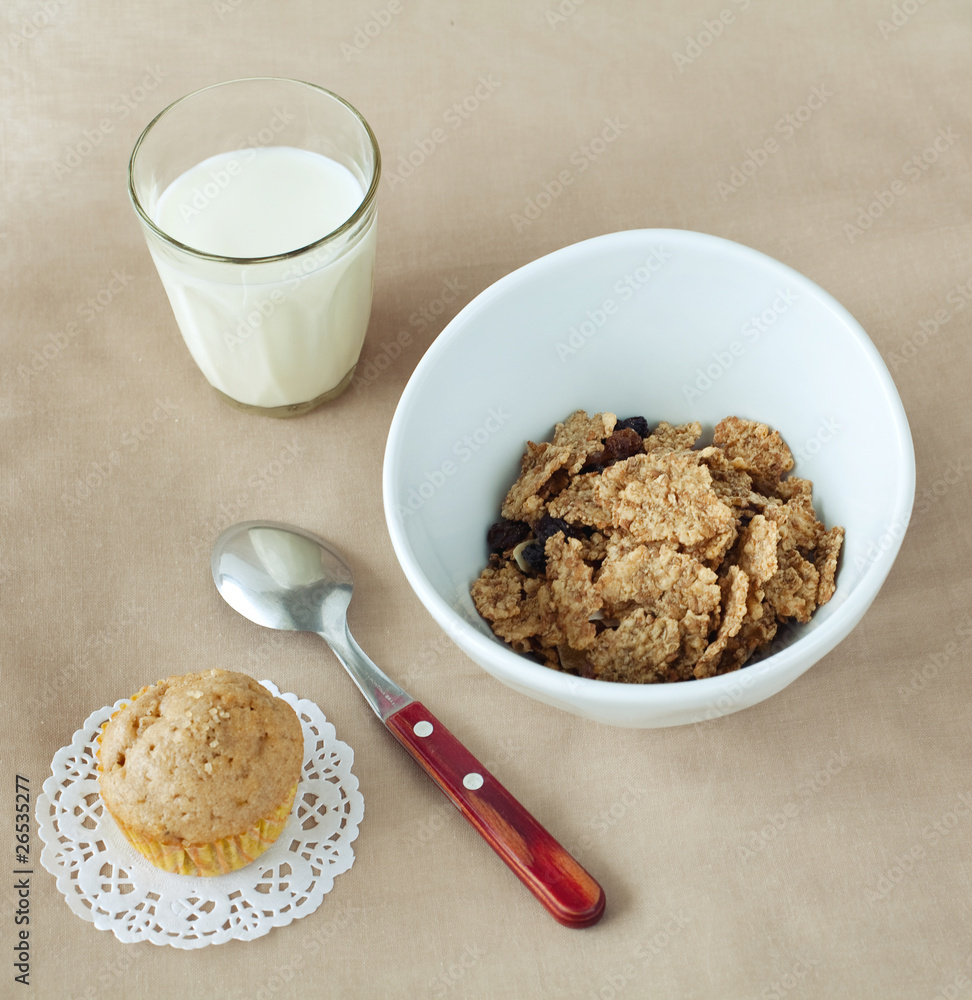 bowl of cornflakes, muffin and glass of milk on beige tablecloth bowl of cornflakes, muffin and glass of milk on beige tablecloth