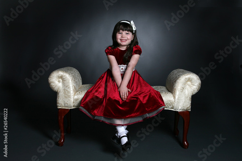pretty little girl in red holiday dress on white bench