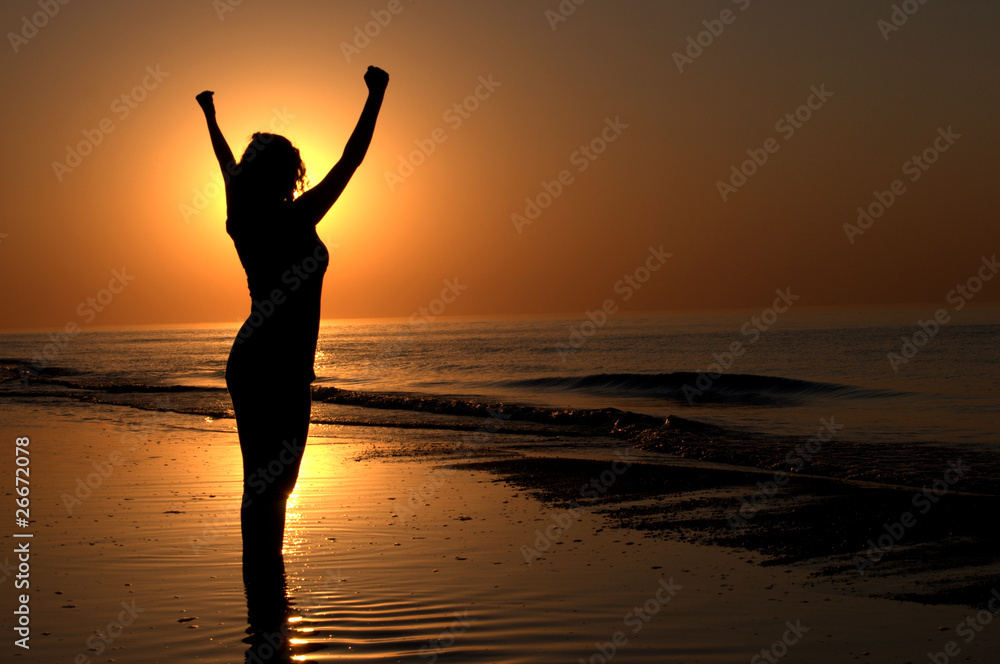 Silhouette of a woman showing achievement on a beach sunset