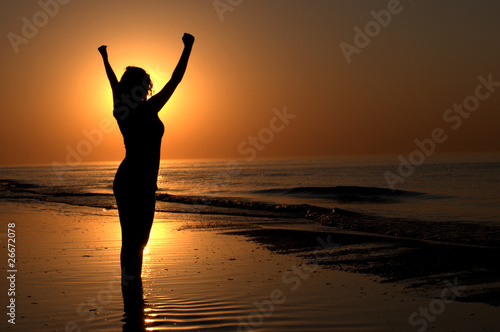 Silhouette of a woman showing achievement on a beach sunset