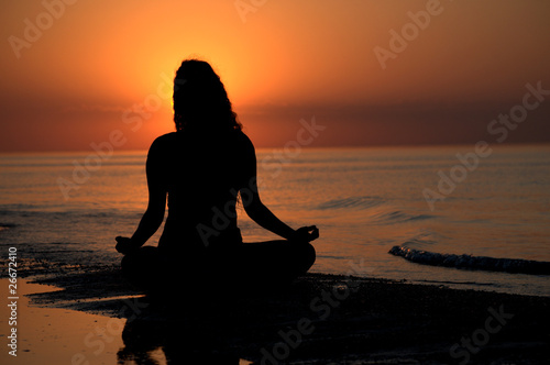 Silhouette of a woman doing yoga by the sunset on the beach