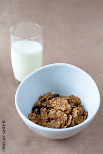 bowl of cornflakes and glass of milk on beige tablecloth